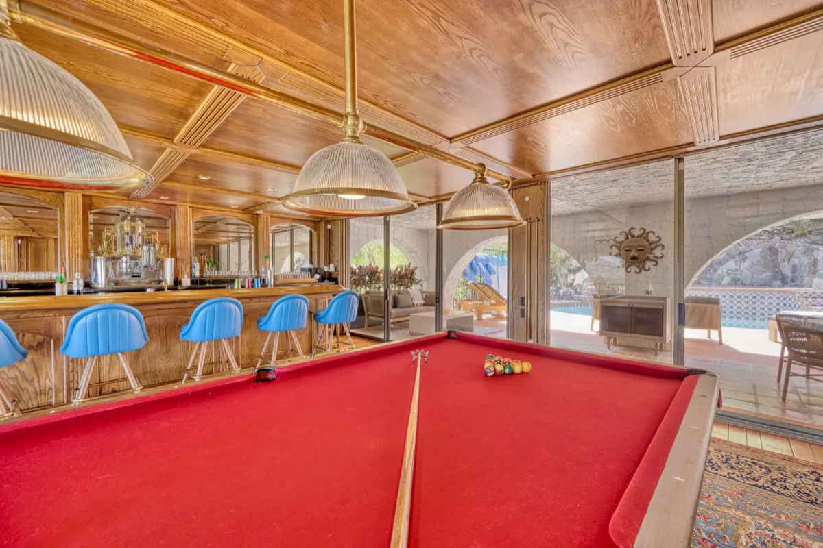 The wood-panelled saloon with a red billiards table, bar seating and glass doors opening to the pool.